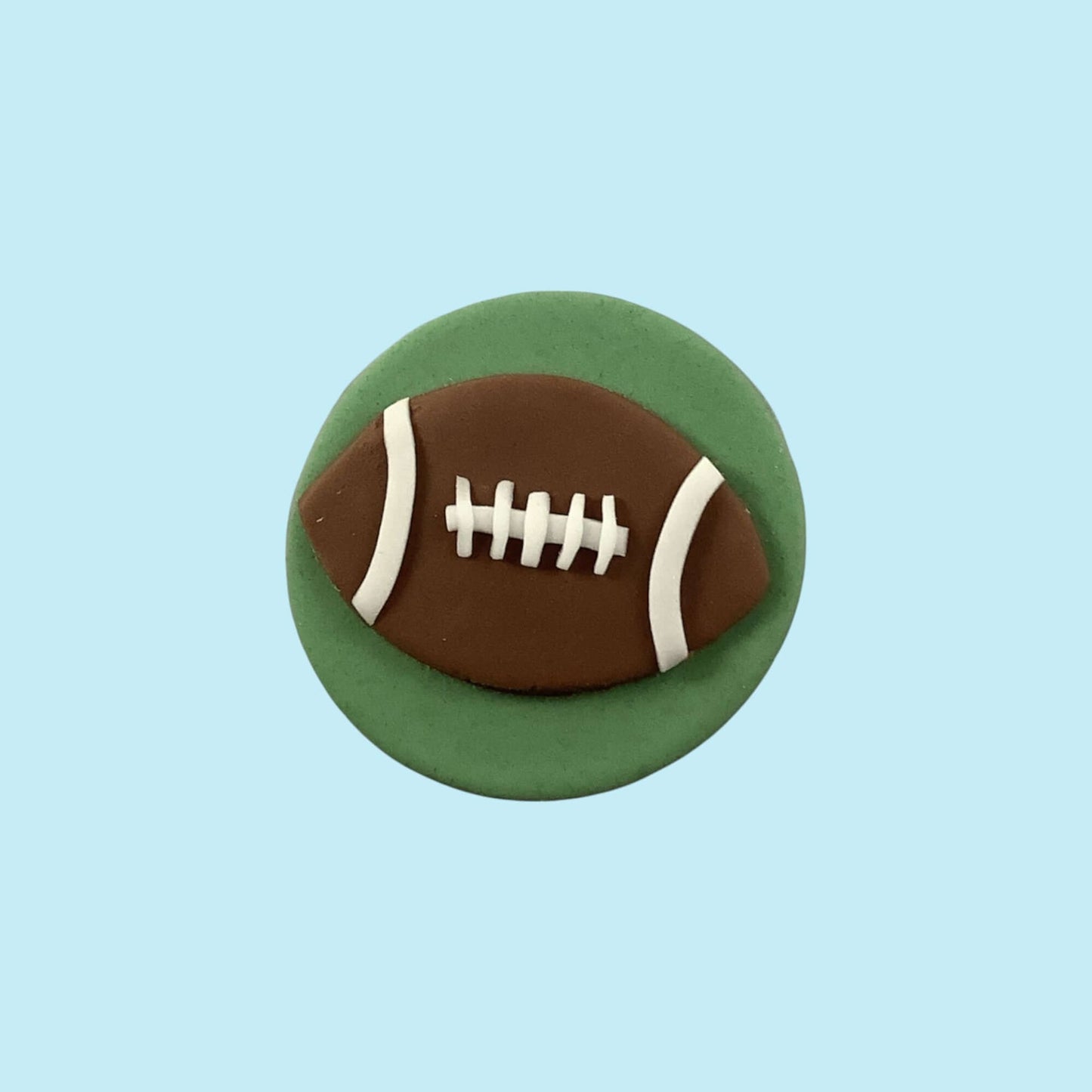 Decorative fondant football on a green round piece against a light blue background