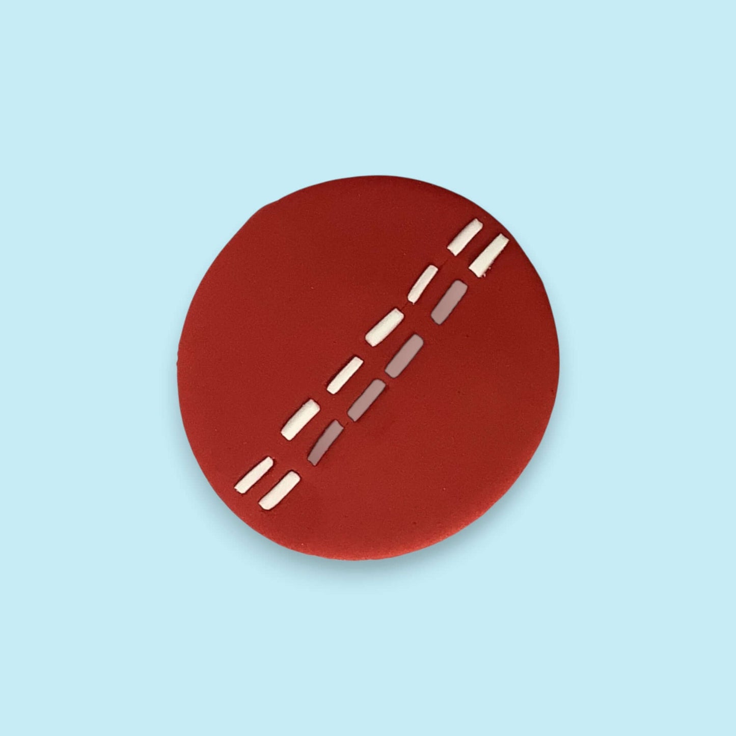 Red circular cricket ball cupcake topper with white lines on a light blue background