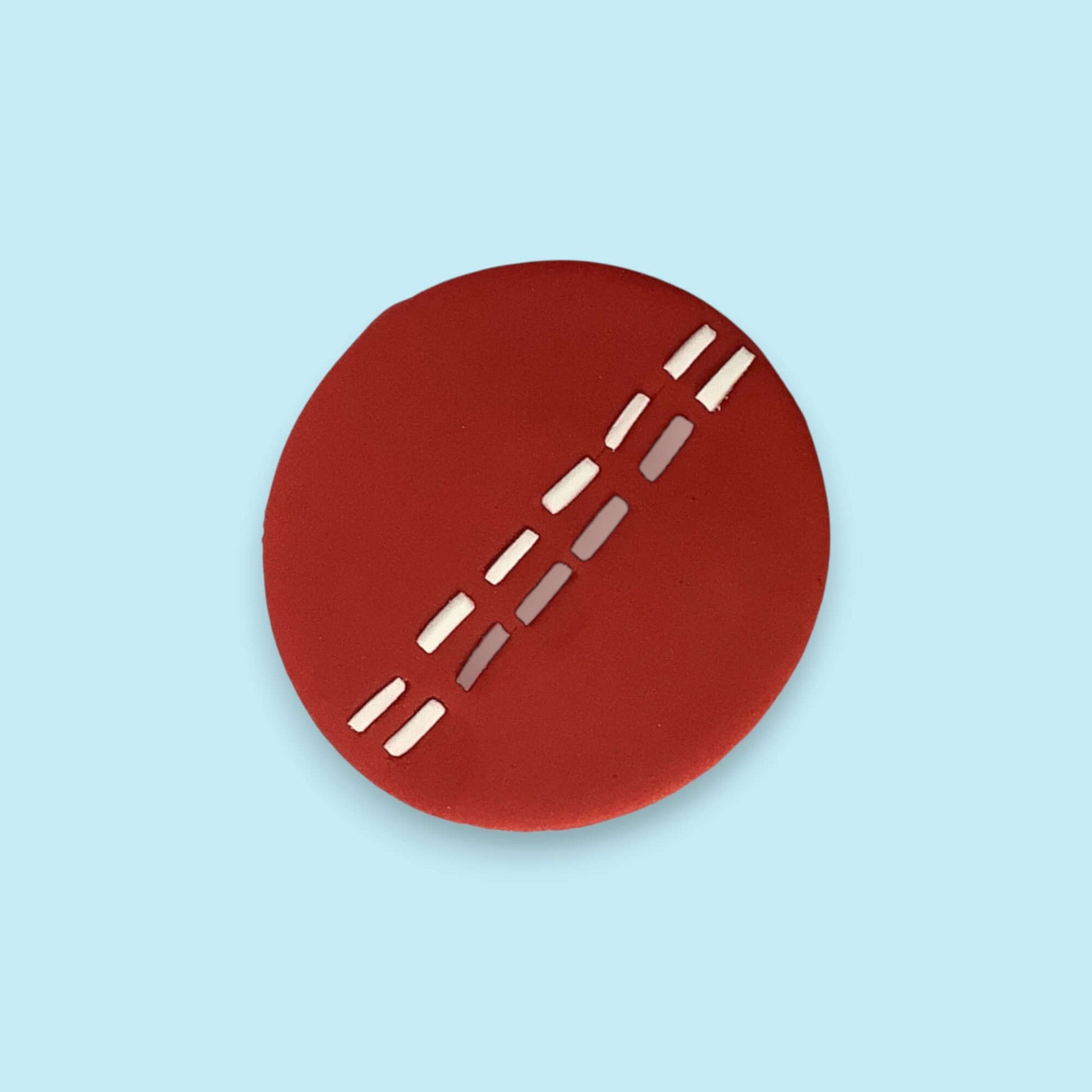 Red circular cricket ball cupcake topper with white lines on a light blue background